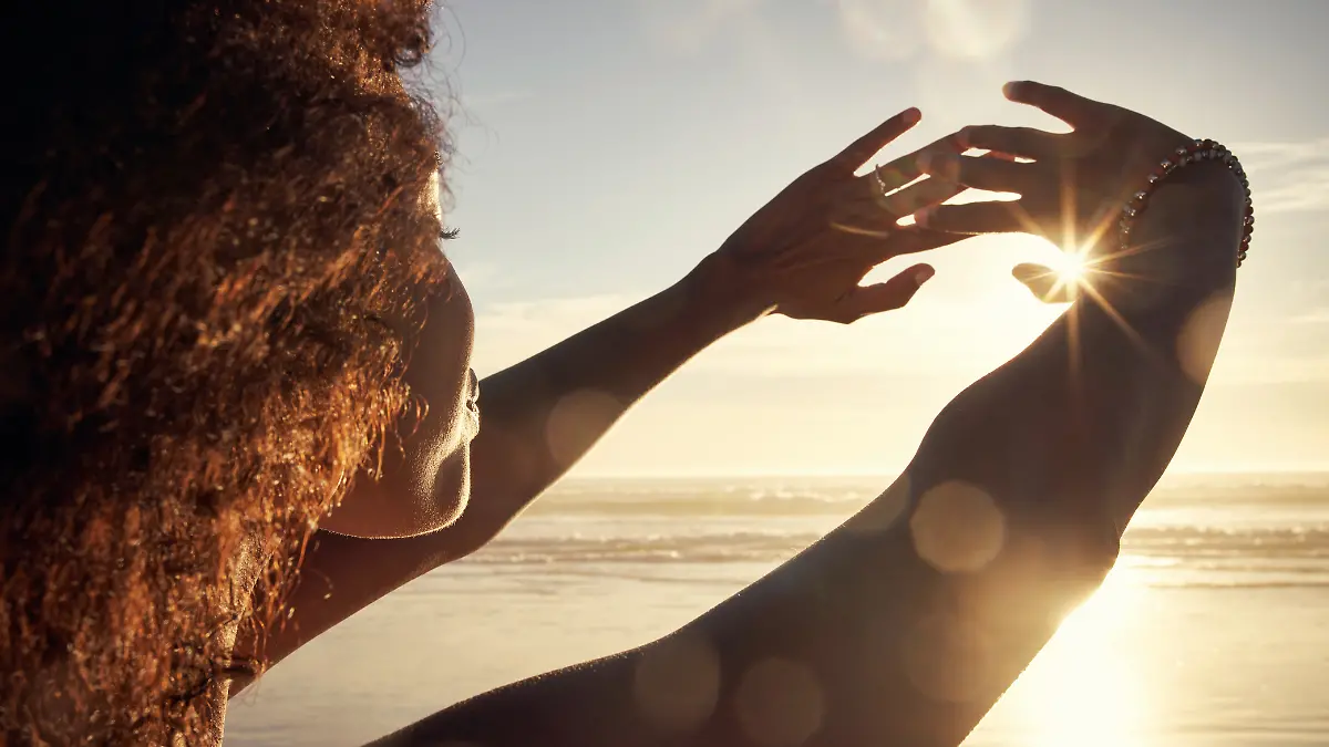 Eine Frau am Meer streckt ihre Arme zur Sonne hin.