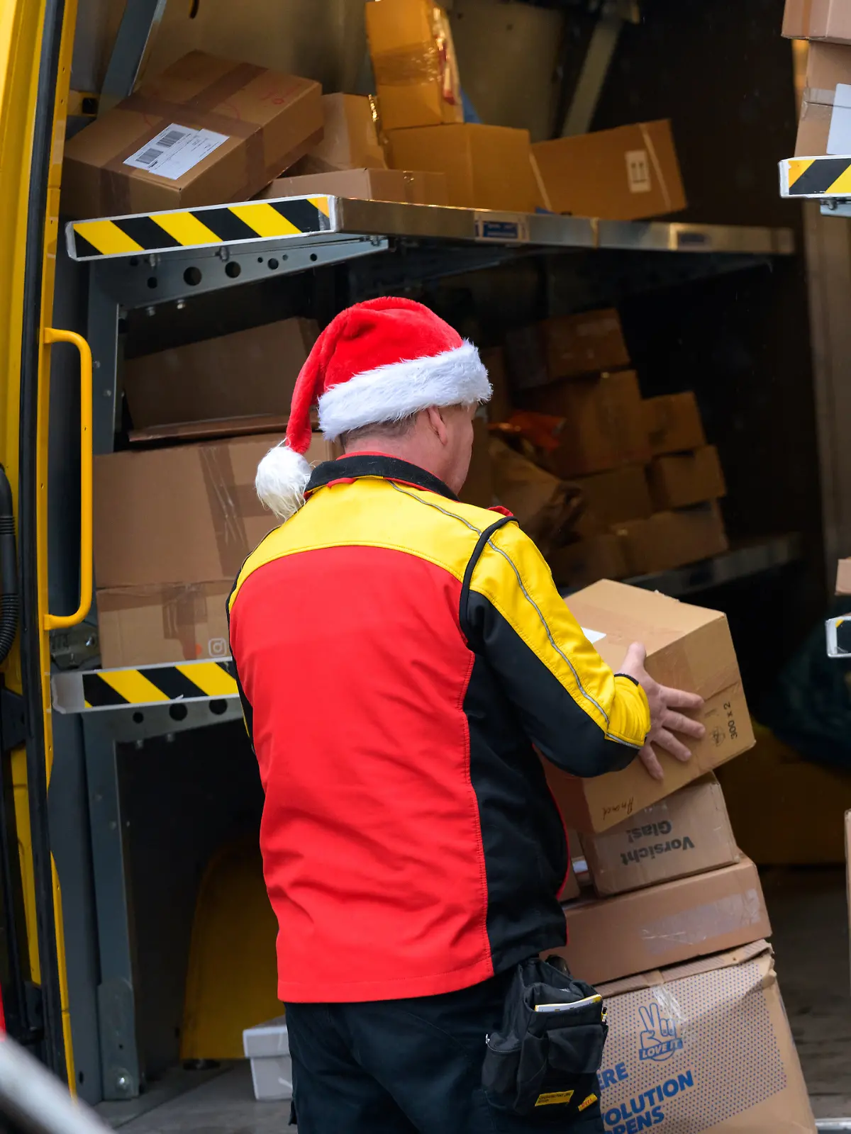 Ein Paketbote des Paketdienstes DHL sortiert mit einer Weihnachtsmütze auf dem Kopf die Pakete in seinem Transporter.