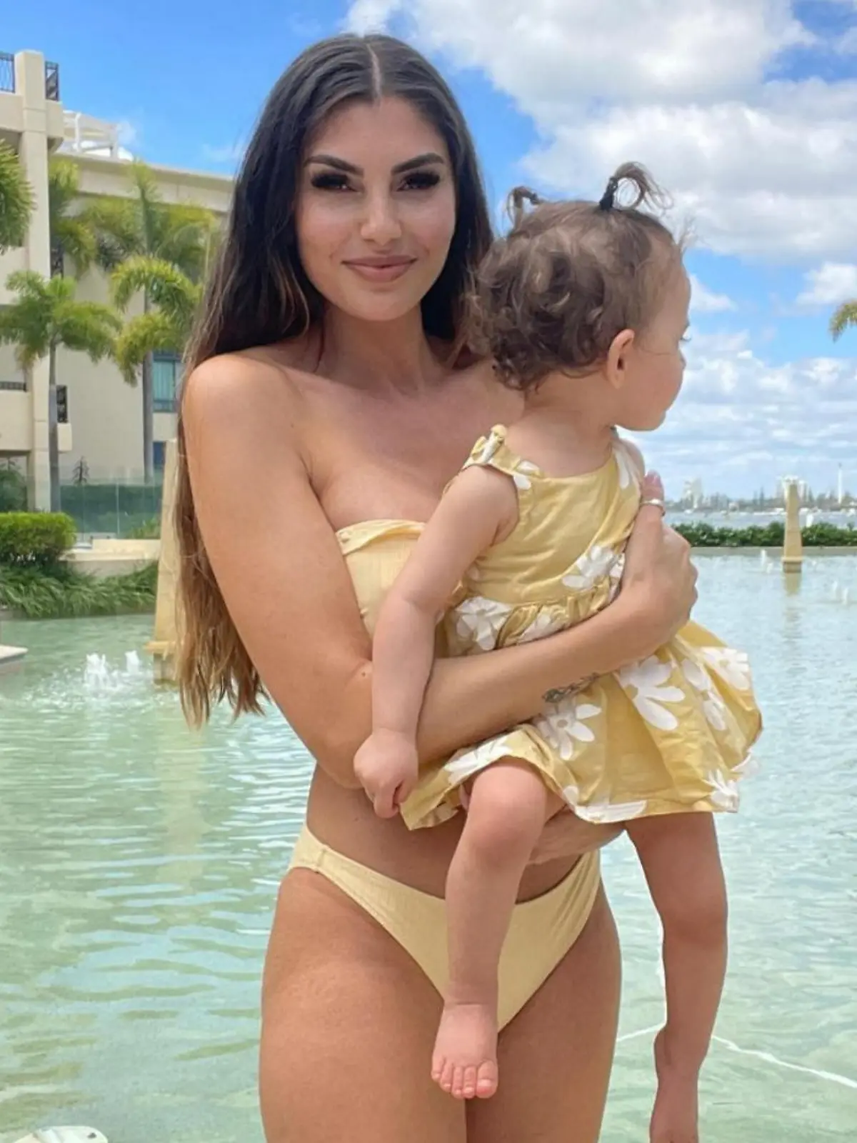 Yeliz Koc posiert mit Tochter Snow Elanie auf dem Arm vor einem Pool.