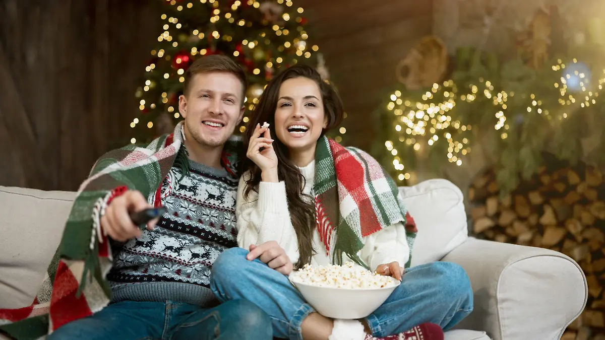 Pärchen sitzt lachend auf dem Sofa und isst Popcorn