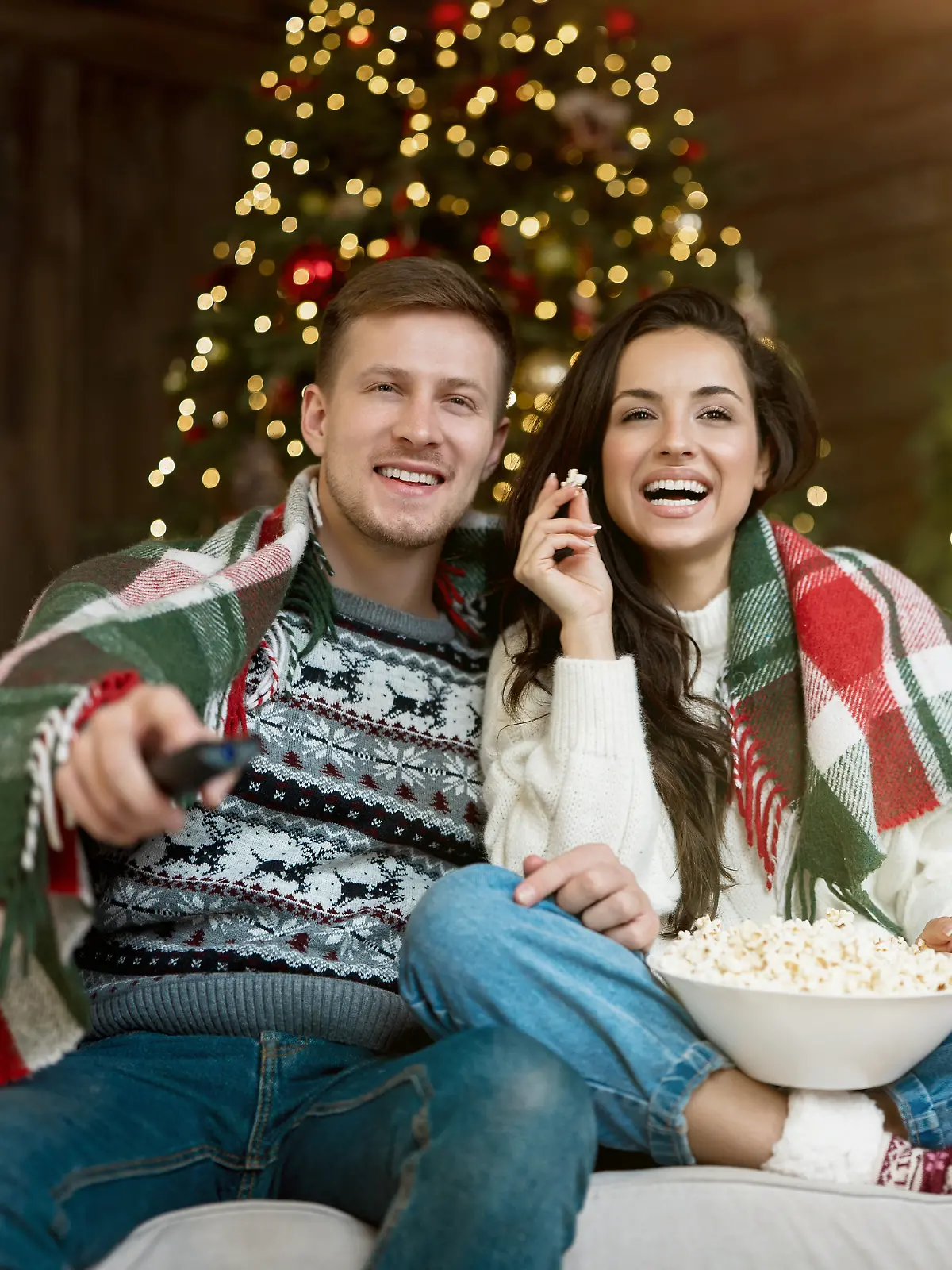 Pärchen sitzt lachend auf dem Sofa und isst Popcorn