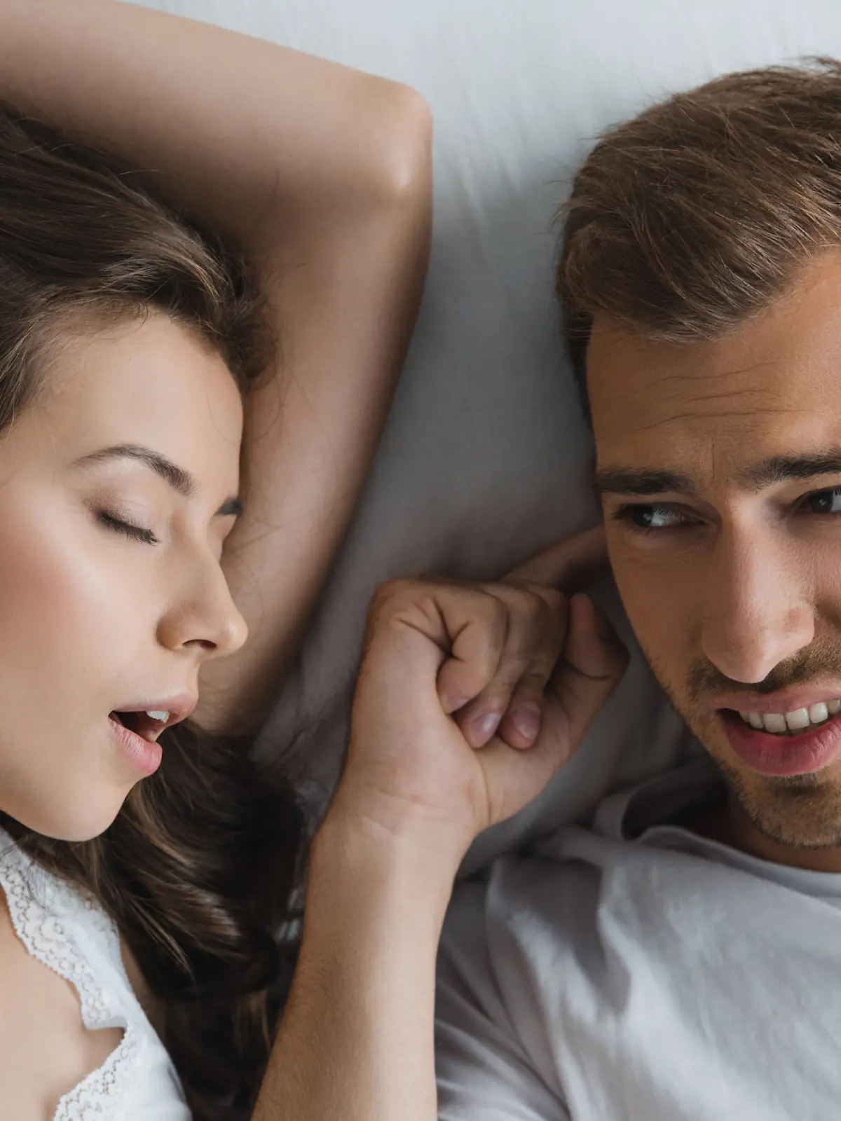Mann liegt neben schnarchender Frau im Bett und hält sich die Ohren zu