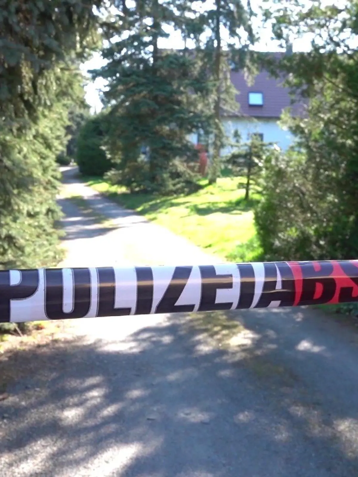 Vor der Einfahrt des Einfamilienhaus hängt eine Polizeiabsperrung.