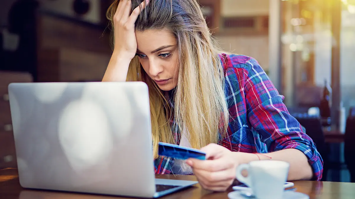 Frau sitzt verzweifelt vor Laptop mit Kreditkarte in der Hand.