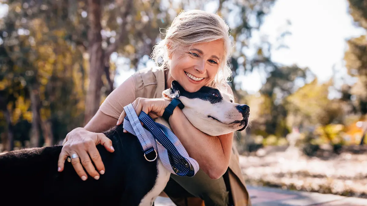Happy senior woman enjoying walk in nature and embracing pet dog in forest park