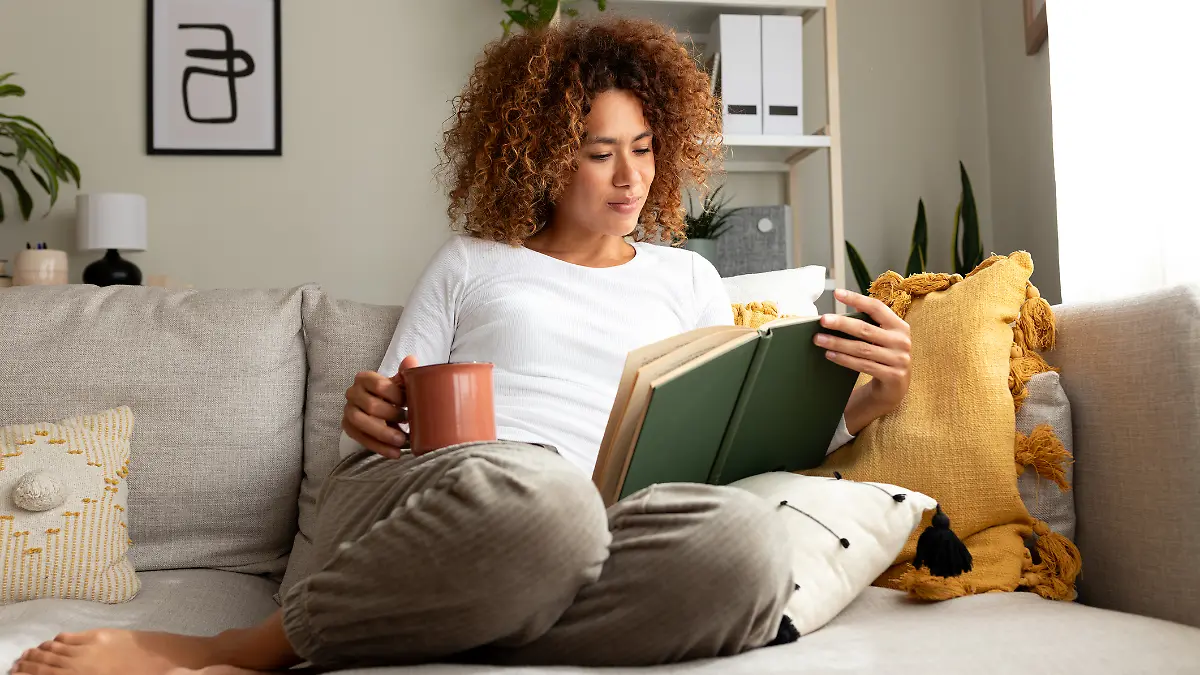 Frau sitzt auf Sofa und liest ein Buch zur Persönlichkeitsentwicklung.