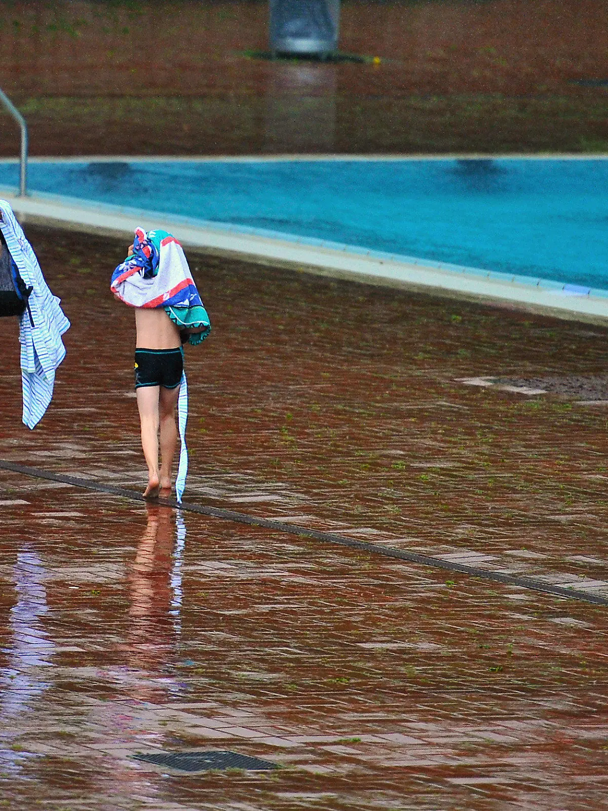 Eine Frau und ein Kind flüchten am Donnerstag (19.07.2012) im Prinzenbad in Berlin vor dem Regen. Immer wieder kam es im Laufe des Tage zu heftigen Schauern. Foto: Hannibal dpa/lbn  +++(c) dpa - Bildfunk+++