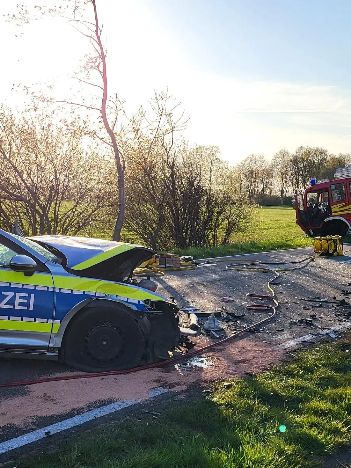 19.04.2022, Niedersachsen, Hoogstede: Ein beschädigtes Polizeiauto und ein Einsatzfahrzeug der Feuerwehr stehen am Unfallort. Bei einem Frontalzusammenstoß zwischen Polizei und Feuerwehr bei Hoogstede im Landkreis Grafschaft Bentheim auf dem Weg zu einem Brand sind zwei Polizisten verletzt worden. Foto: ---/Nord-West-Media TV /dpa +++ dpa-Bildfunk +++
