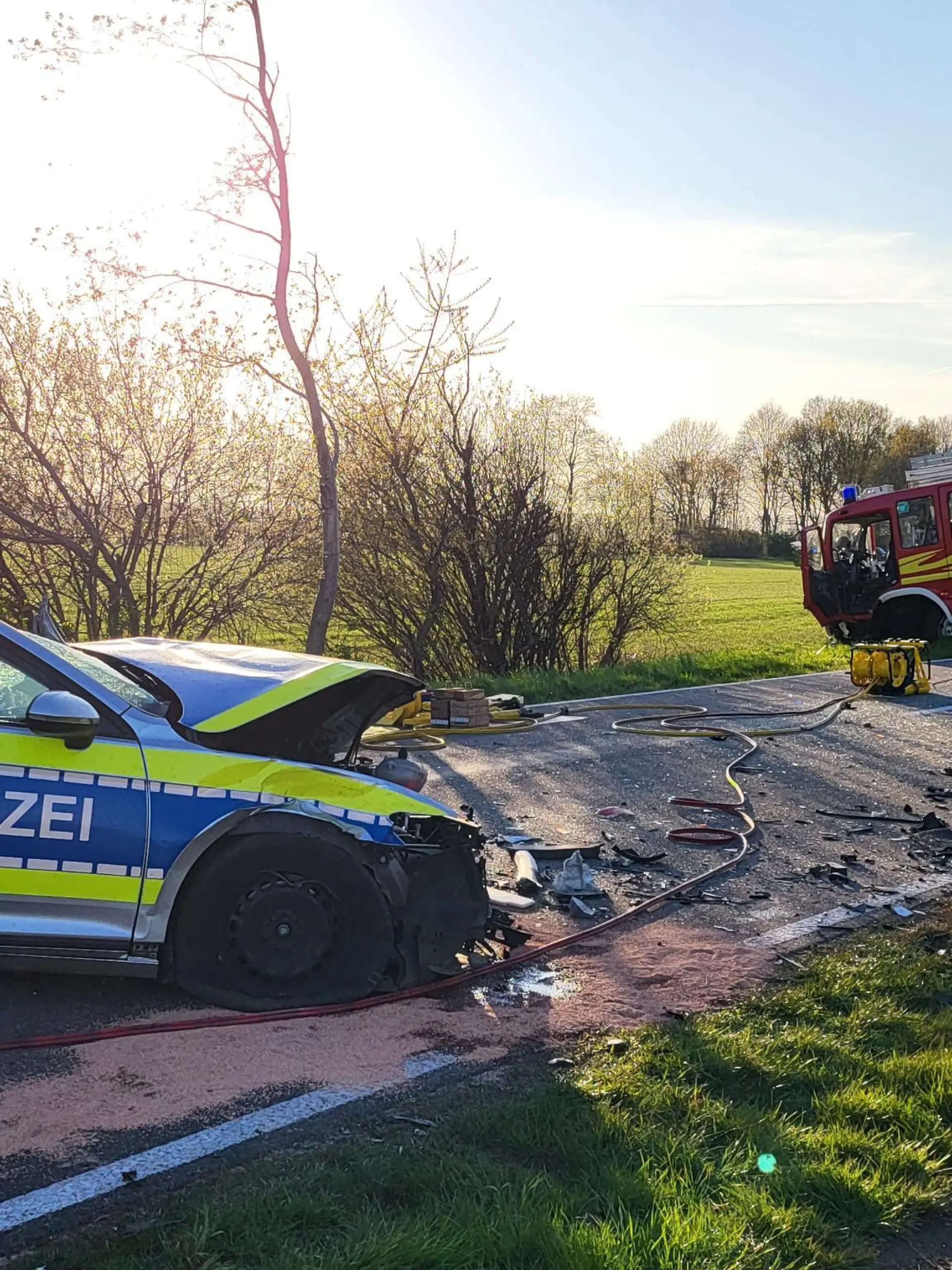 19.04.2022, Niedersachsen, Hoogstede: Ein beschädigtes Polizeiauto und ein Einsatzfahrzeug der Feuerwehr stehen am Unfallort. Bei einem Frontalzusammenstoß zwischen Polizei und Feuerwehr bei Hoogstede im Landkreis Grafschaft Bentheim auf dem Weg zu einem Brand sind zwei Polizisten verletzt worden. Foto: ---/Nord-West-Media TV /dpa +++ dpa-Bildfunk +++