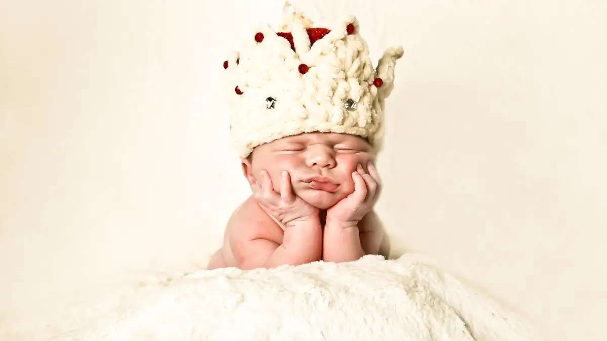 Portrait of a newborn baby wearing a crown, napping on hands, propped on his elbow.