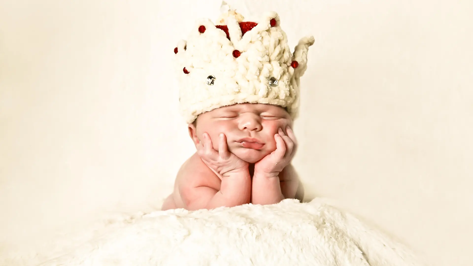 Portrait of a newborn baby wearing a crown, napping on hands, propped on his elbow.