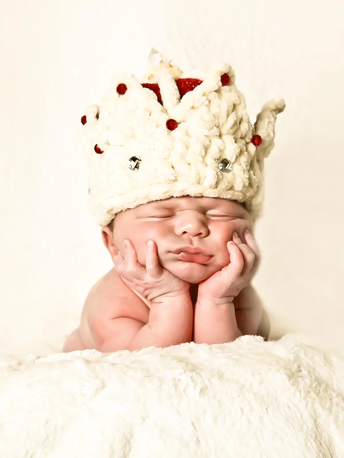 Portrait of a newborn baby wearing a crown, napping on hands, propped on his elbow.