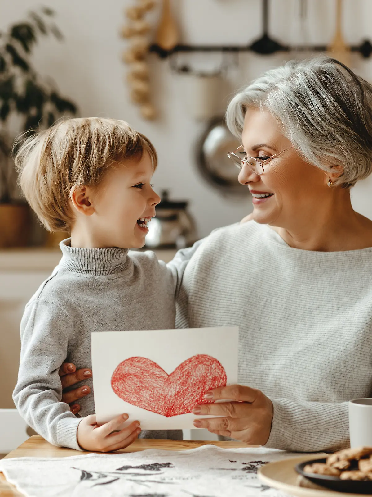 Oma beschäftigt sich mit Kind und hält gemaltes Bild mit Herz in die Kamera