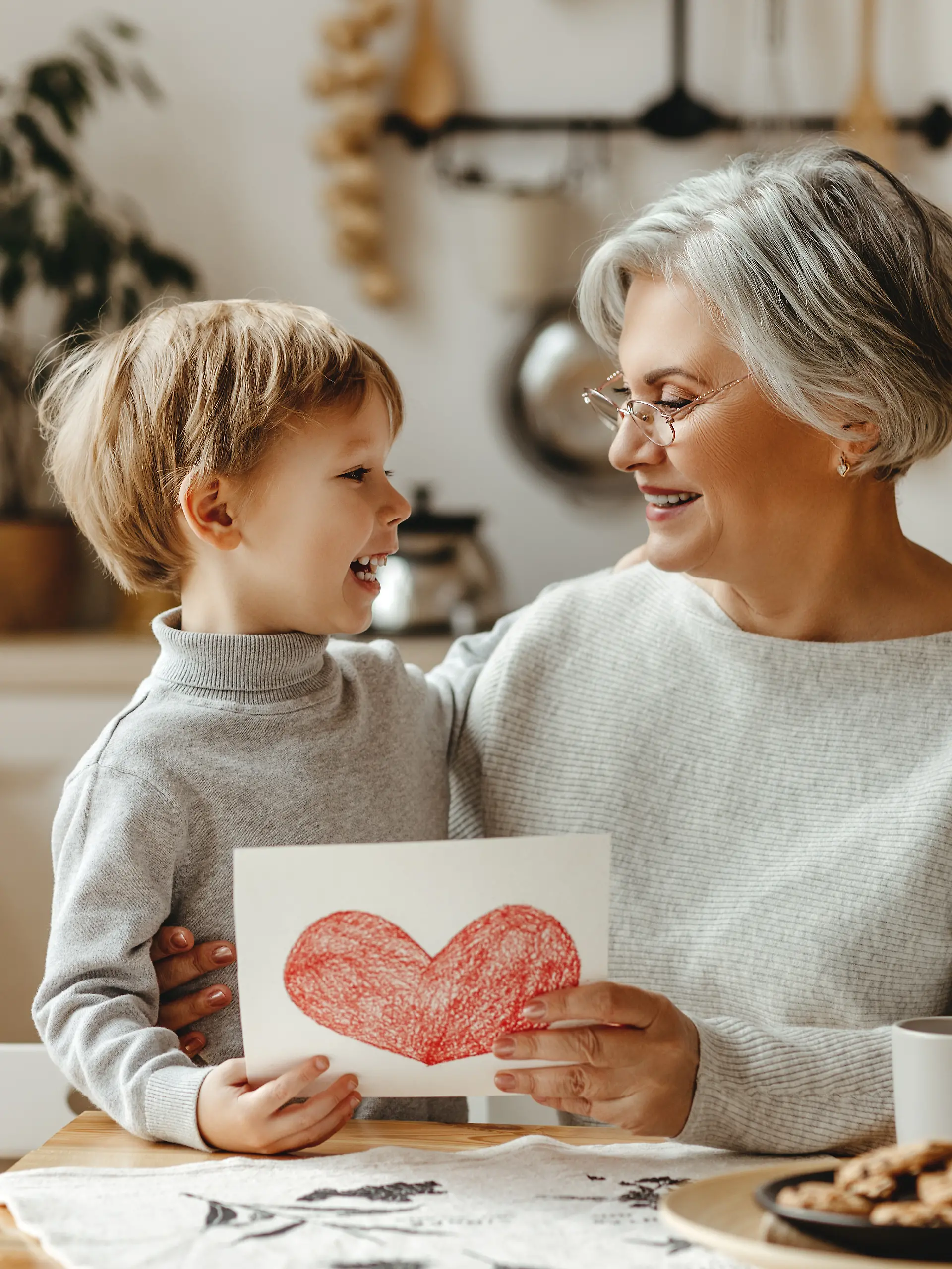 Oma beschäftigt sich mit Kind und hält gemaltes Bild mit Herz in die Kamera