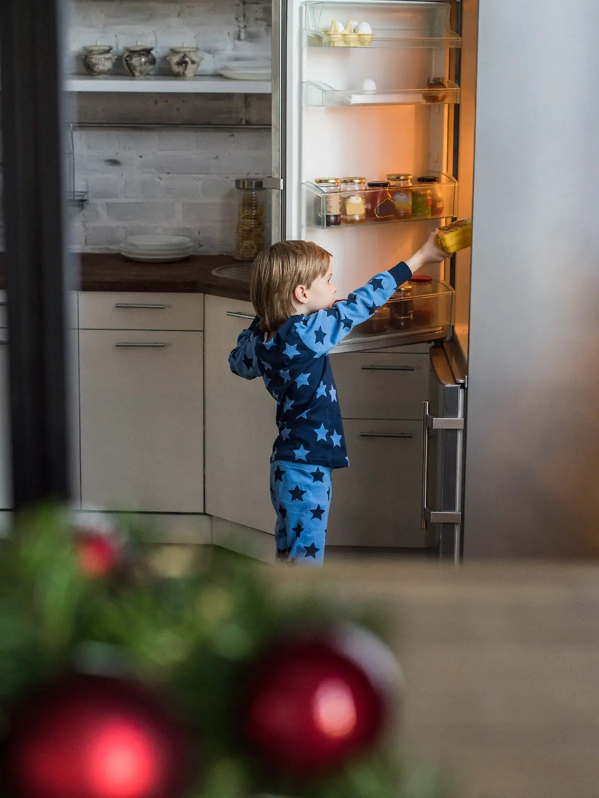 Junge holt sich etwas aus dem geöffneten Kühlschrank