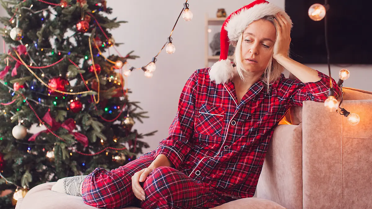 Frau sitzt mit Kater vor dem Weihnachtsbaum.