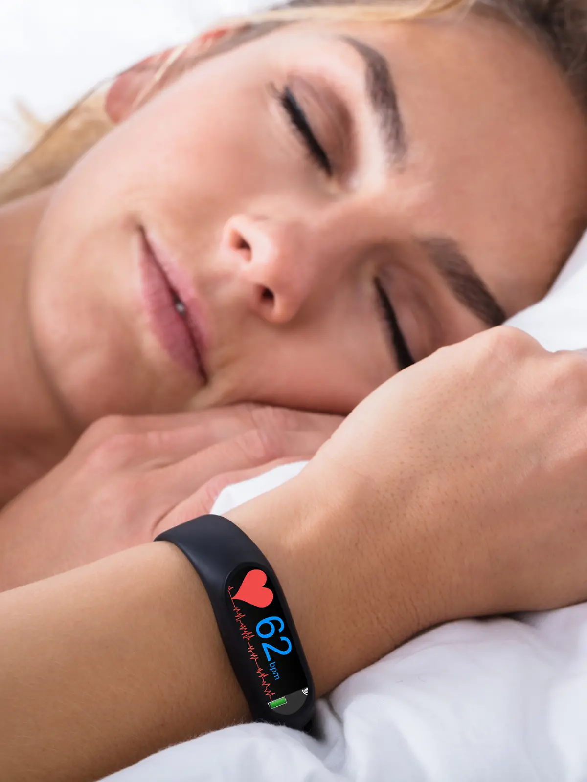 Eine Frau schläft mit einer Smartwatch am Handgelenk, um ihren Rhythmus zu tracken. 