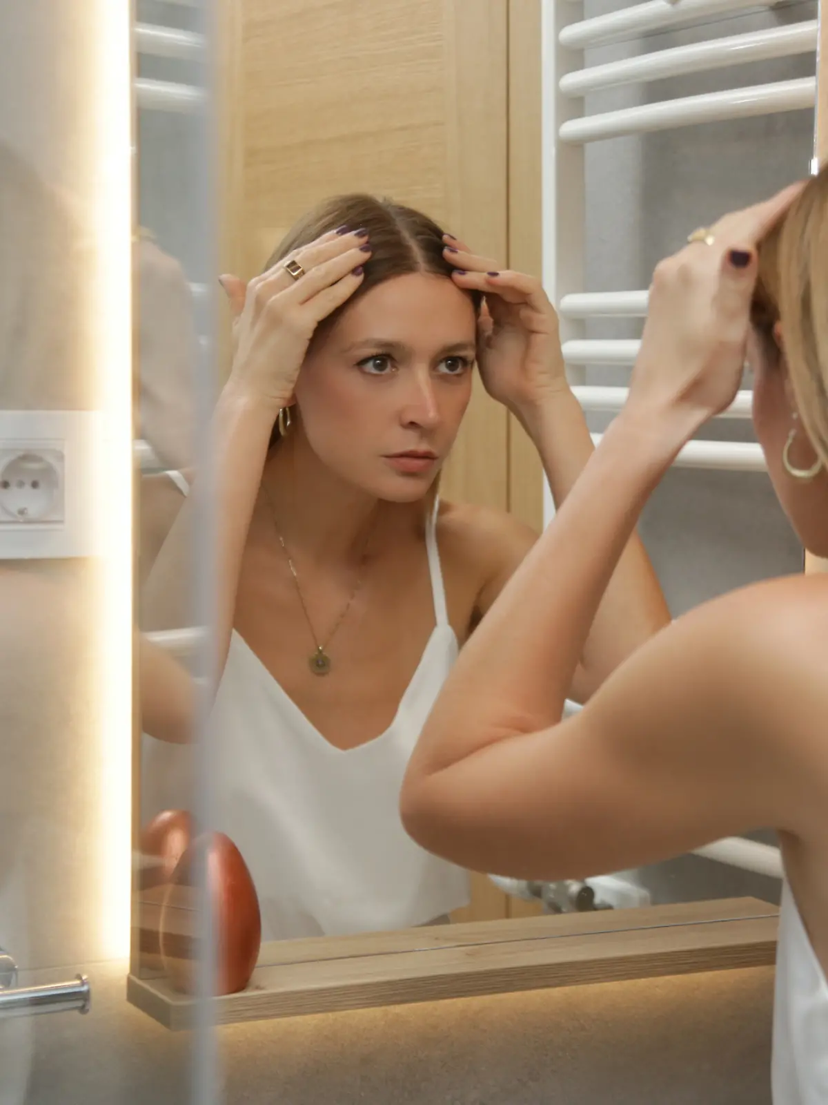 Eine Frau begutachtet sich, ihre Haut und Haare im Spiegel.