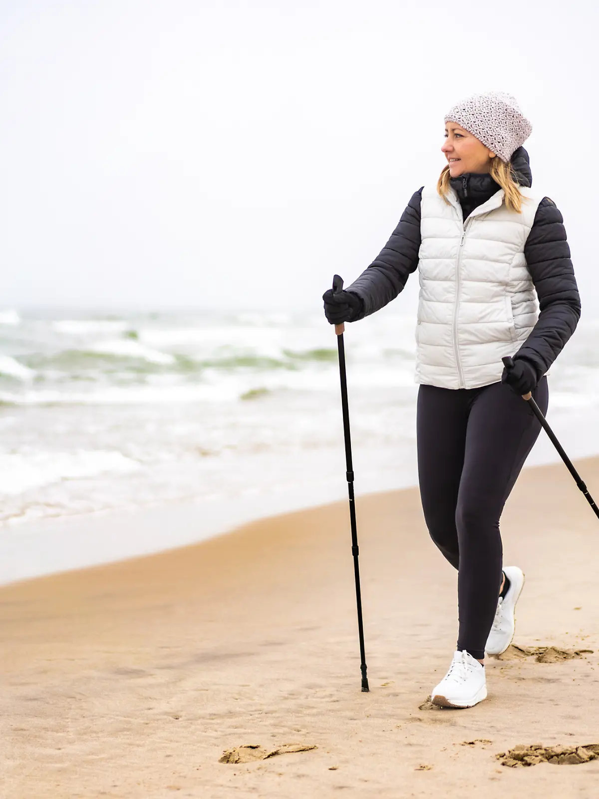 Eine junge Frau betreibt Nordic Walking im Winter am Strand.