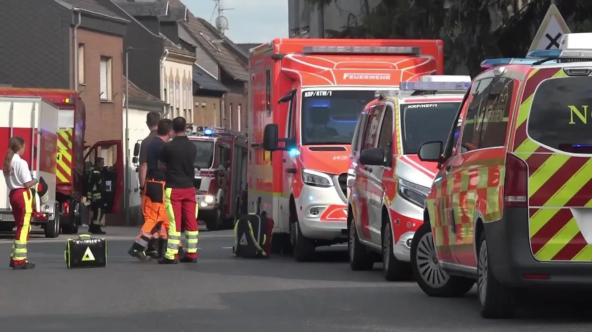 Einsatzkräfte von Rettungsdienst und Feuerwehr stehen in der Straße an der Unfallstelle.
