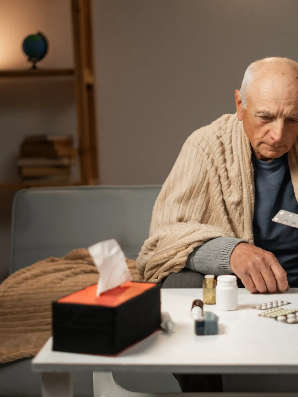 Ein kranker Mann sitzt auf dem Sofa und hält Tabletten in den Händen. 