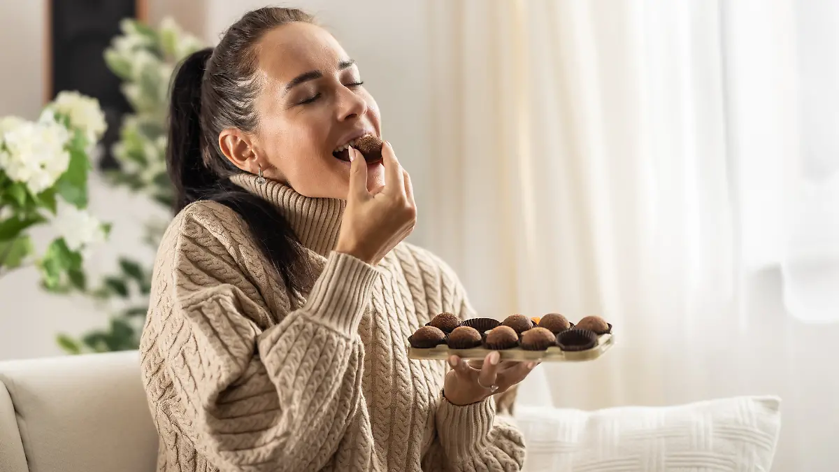 Eine Frau isst auf dem Sofa Pralinen.