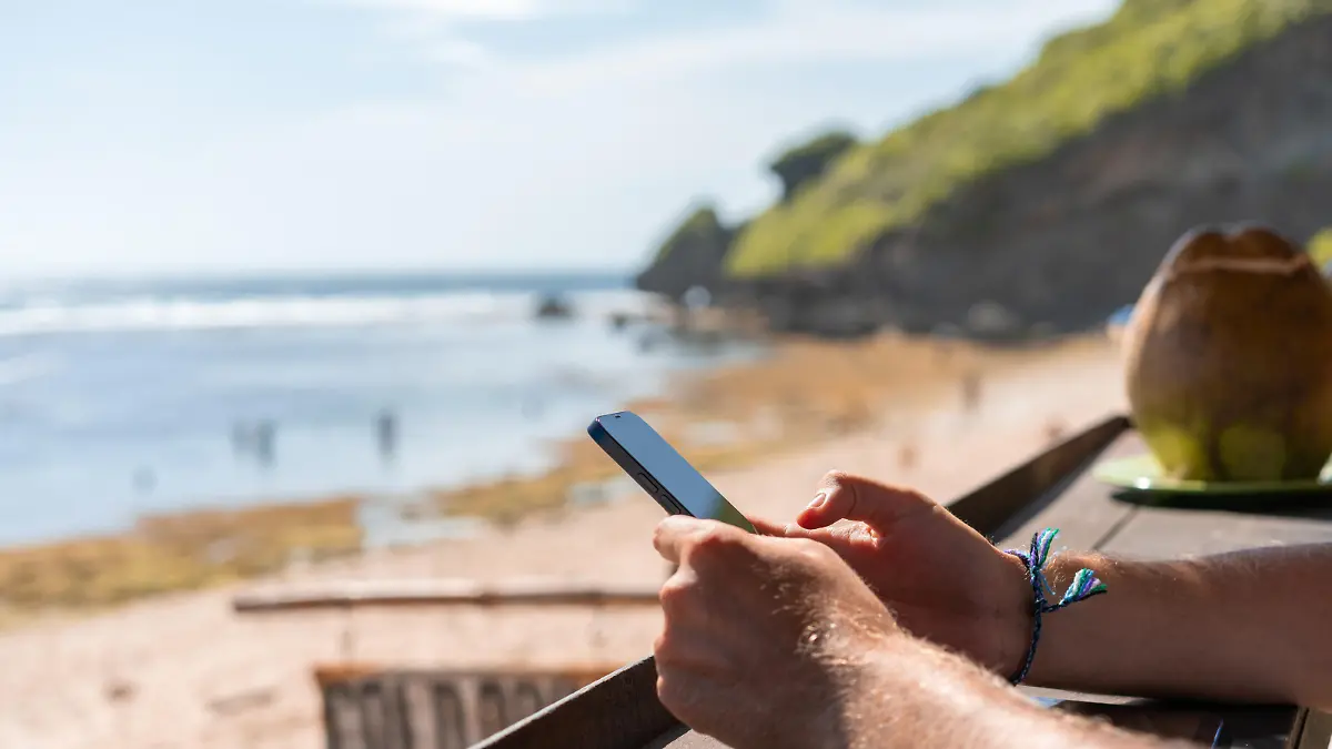 Businessman hands using phone, blurred beach and hills on background. Concept of remote work, online business and traveling
