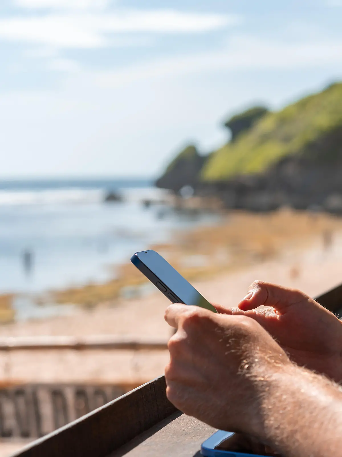 Businessman hands using phone, blurred beach and hills on background. Concept of remote work, online business and traveling