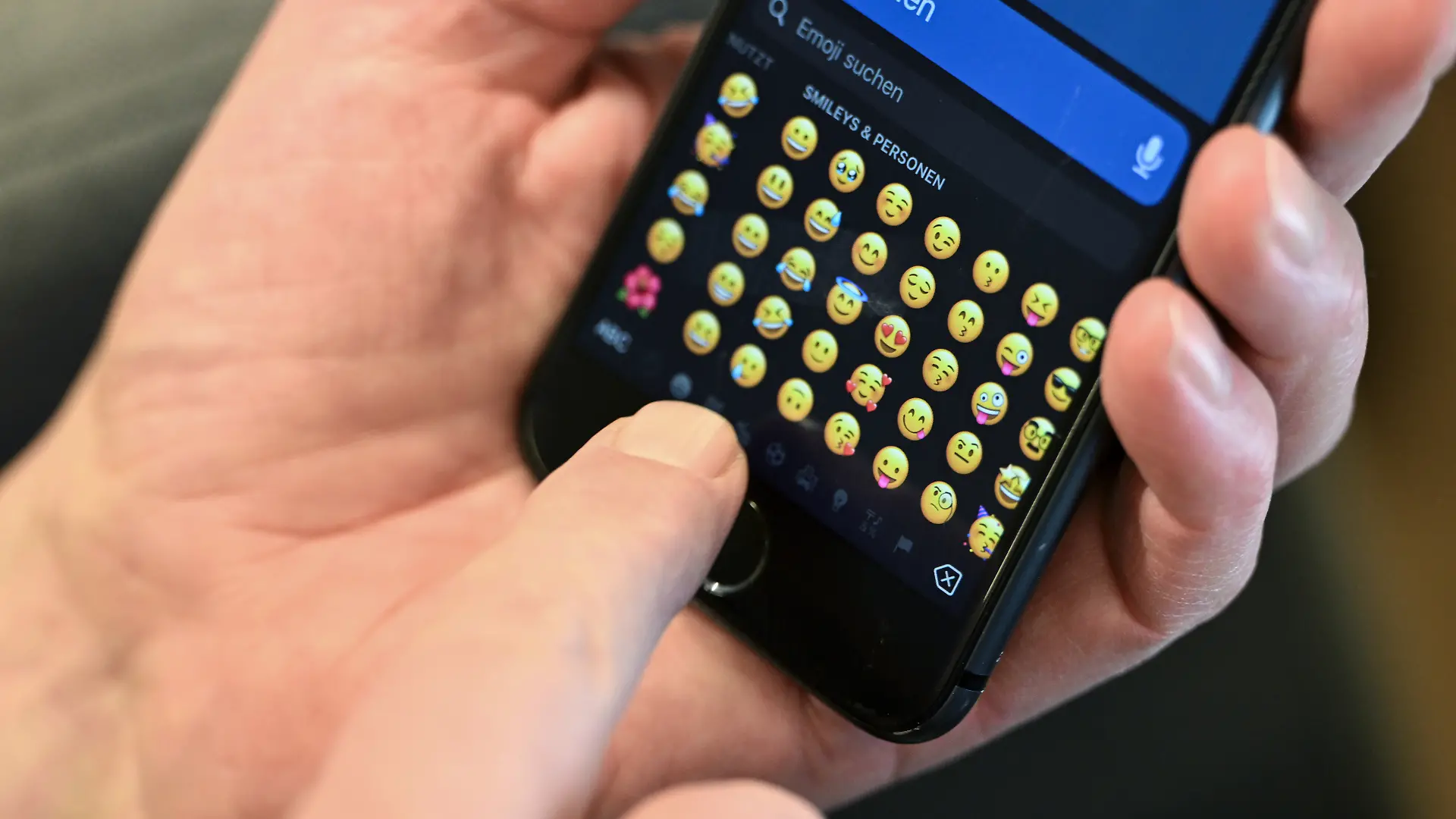 Mann tippt auf Handy Emojis an. 