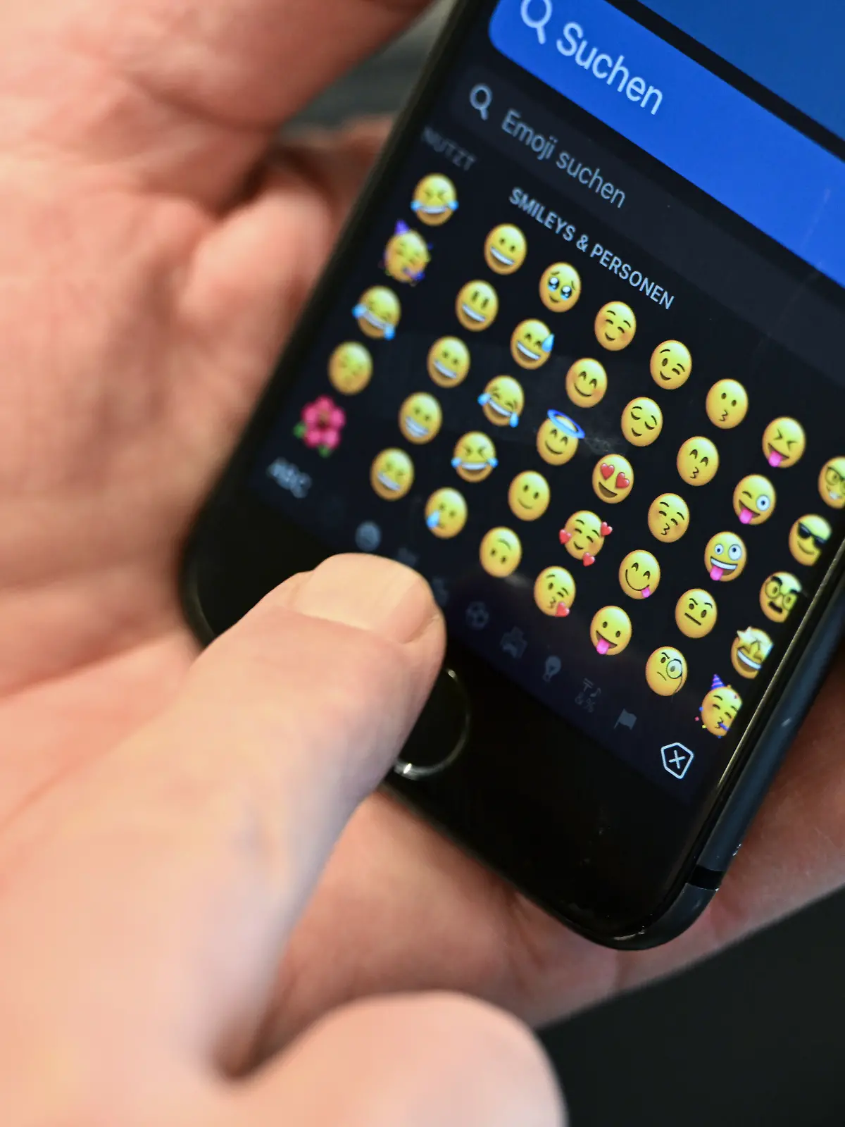 Mann tippt auf Handy Emojis an. 