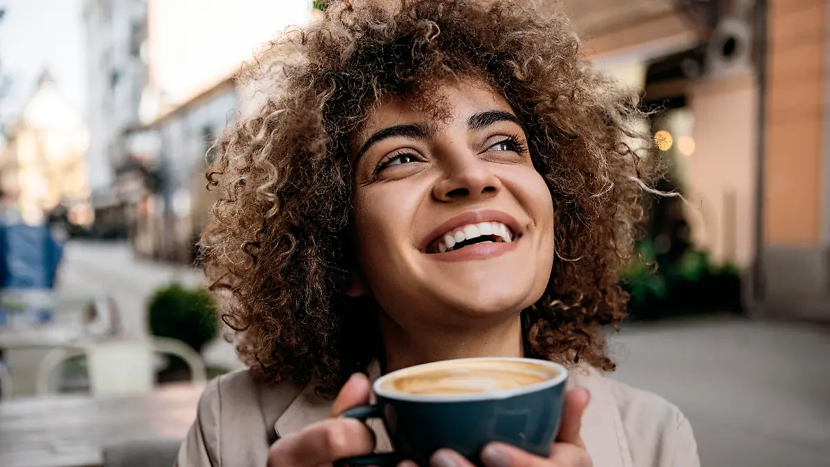 Frau hält eine Kaffeetasse in der Hand und lacht.
