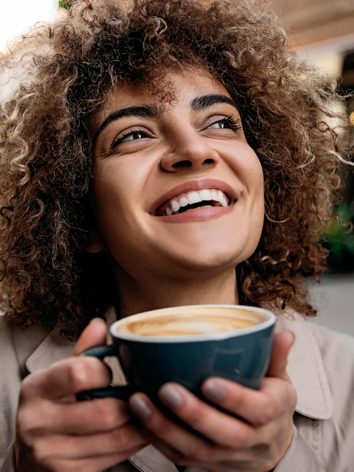 Frau hält eine Kaffeetasse in der Hand und lacht.