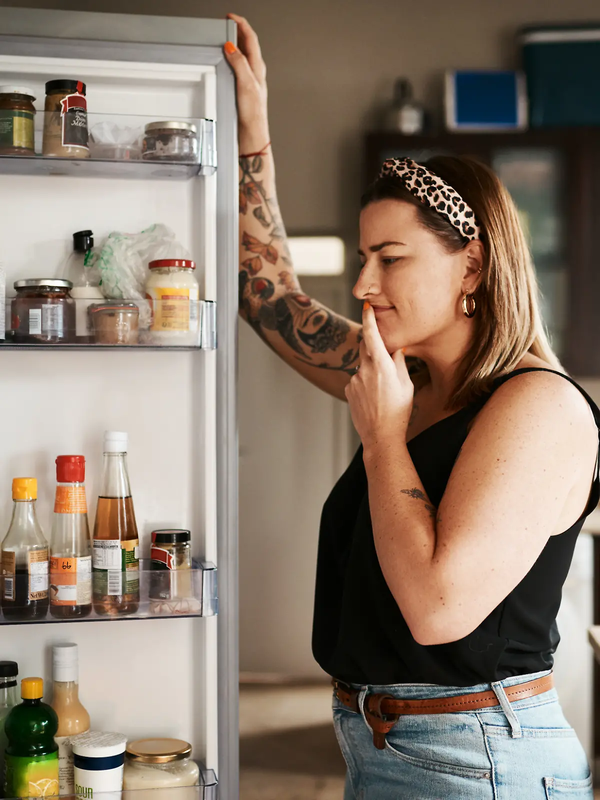 Frau schaut lächelnd in den Kühlschrank.