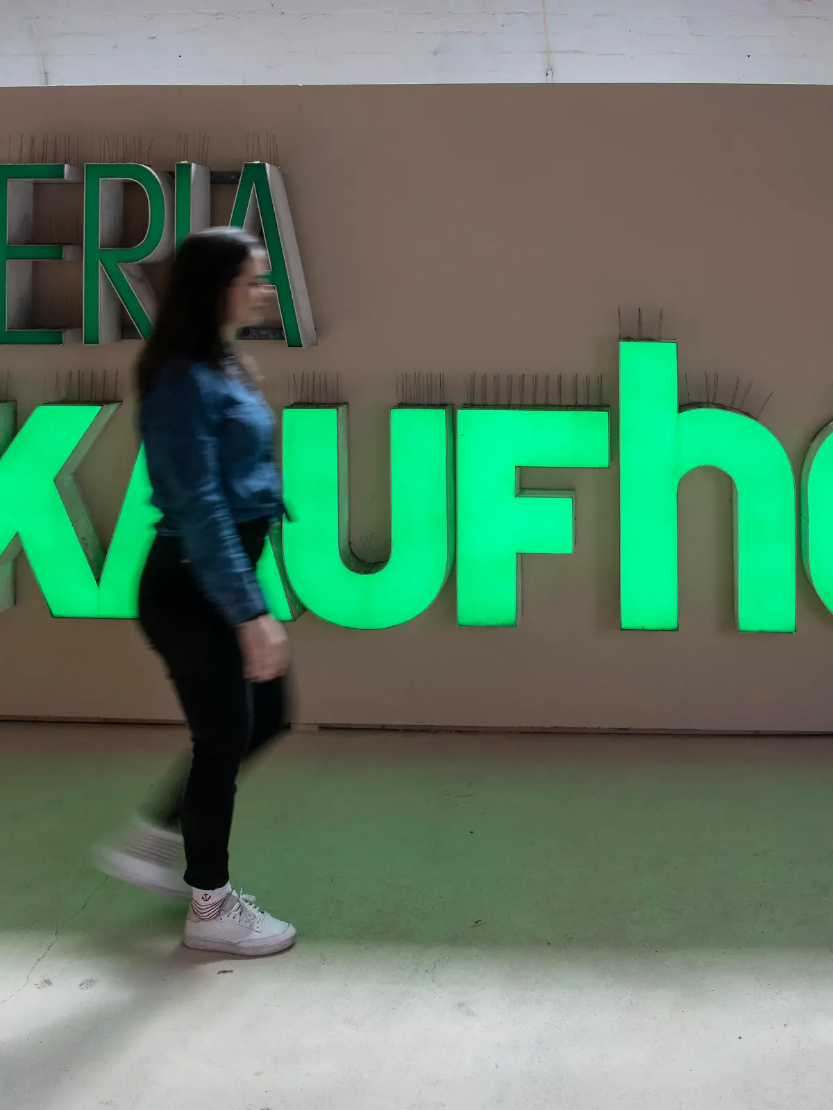 20.05.2023, Berlin: Olivia aus Südafrika geht in der Ausstellung "Final sale · vom Kaufhaus ins Museum" im Buchstabenmuseum an dem Schriftzug Galeria Kaufhof vorbei. In dem Museum gibt es eine neue Ausstellung, die sich mit der Geschichte und der Bedeutung der Schriftzüge bekannter Geschäfte befasst. Foto: Paul Zinken/dpa +++ dpa-Bildfunk +++