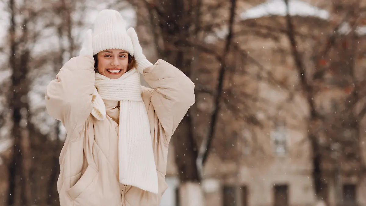Eine junge Frau in weißer Kleidung steht in einer winterlichen Landschaft und lächelt in die Kamera.