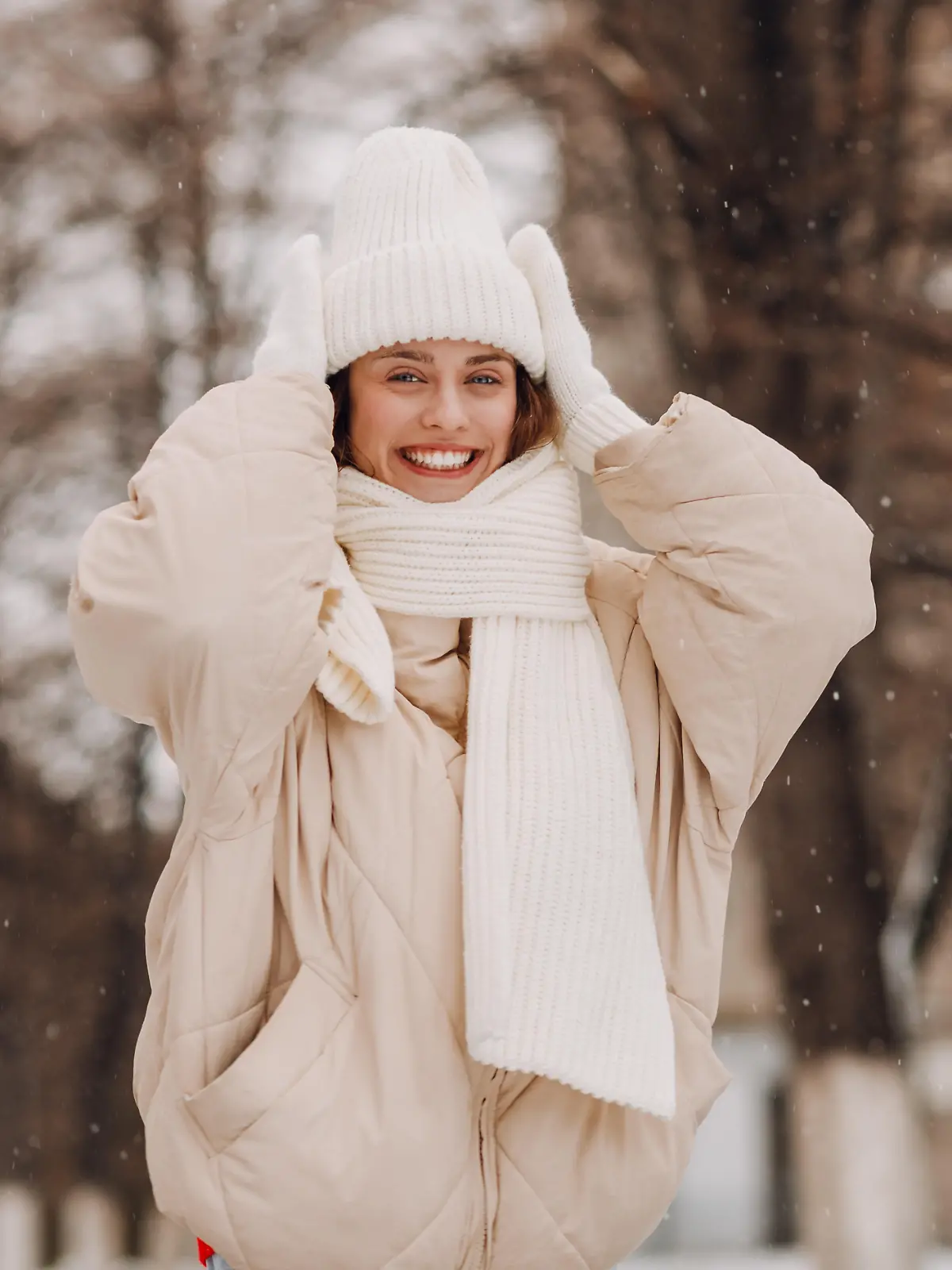 Eine junge Frau in weißer Kleidung steht in einer winterlichen Landschaft und lächelt in die Kamera.