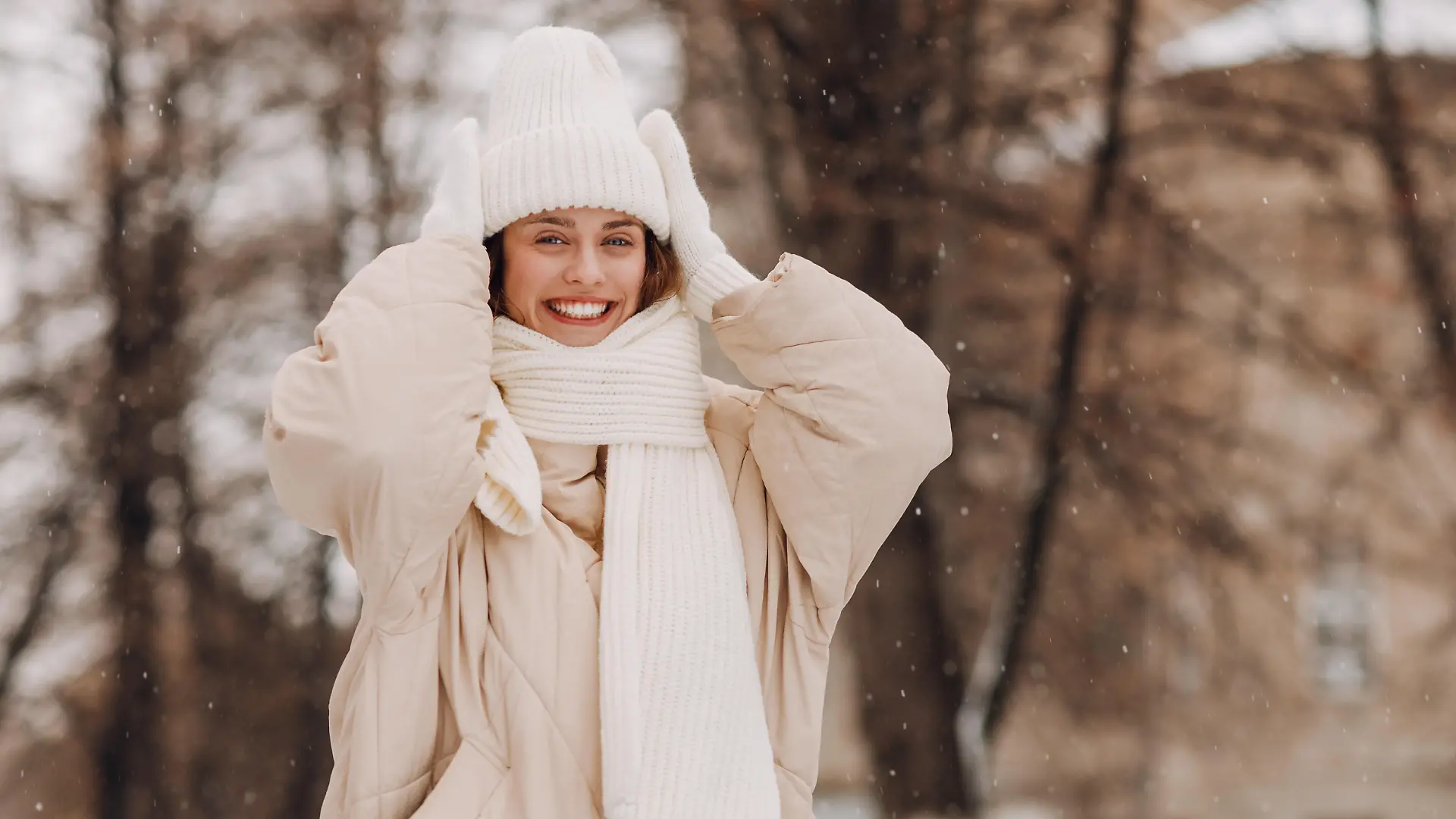 Eine junge Frau in weißer Kleidung steht in einer winterlichen Landschaft und lächelt in die Kamera.