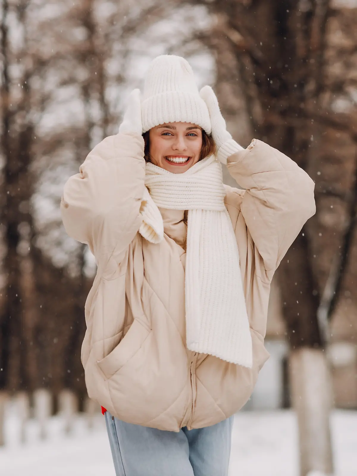 Eine junge Frau in weißer Kleidung steht in einer winterlichen Landschaft und lächelt in die Kamera.