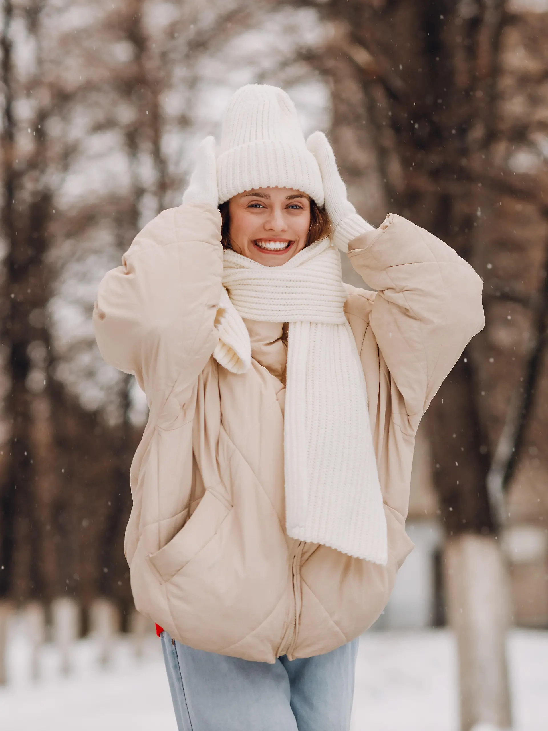 Eine junge Frau in weißer Kleidung steht in einer winterlichen Landschaft und lächelt in die Kamera.
