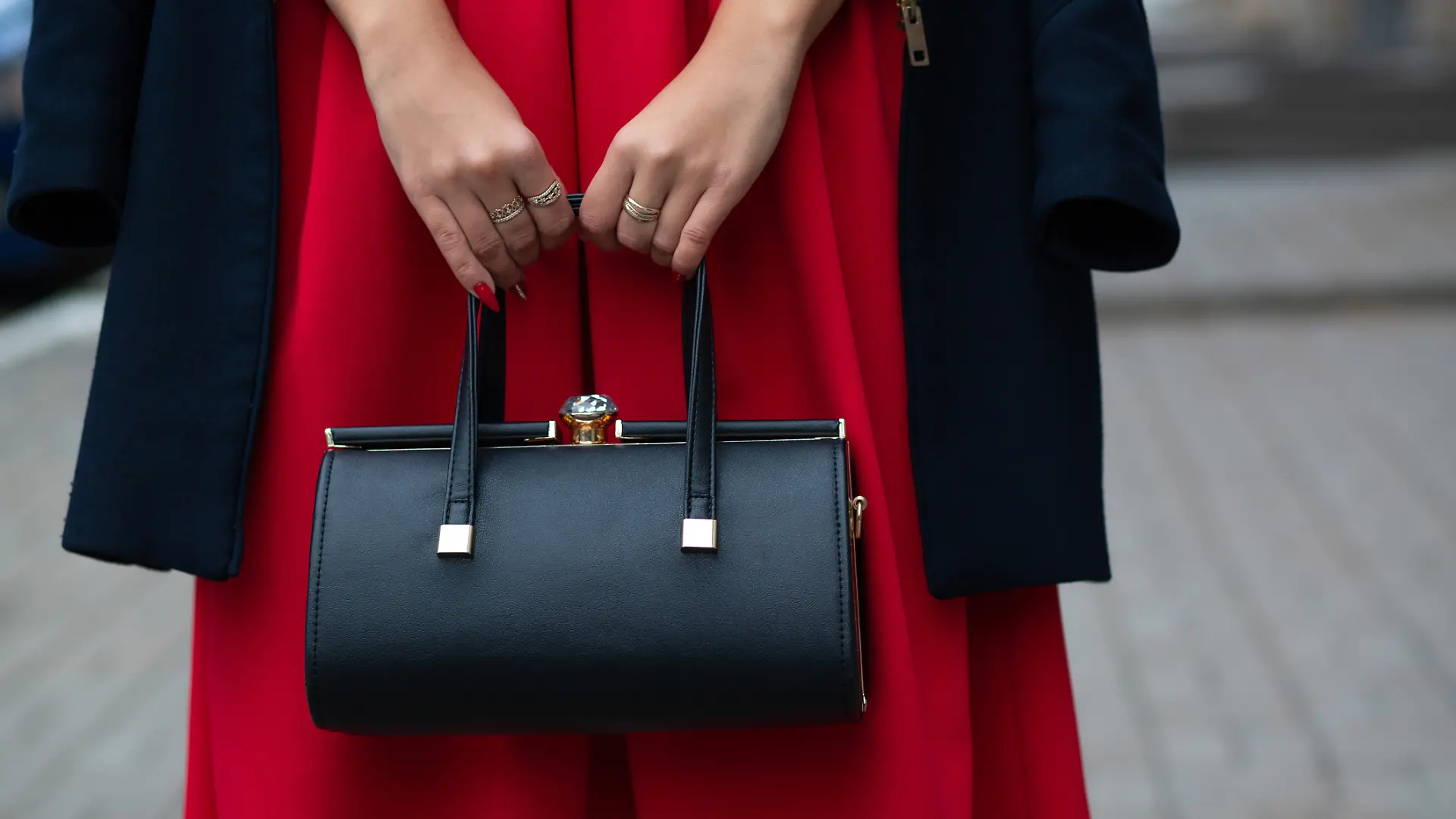 Frau hält schwarze Handtasche in den Händen.