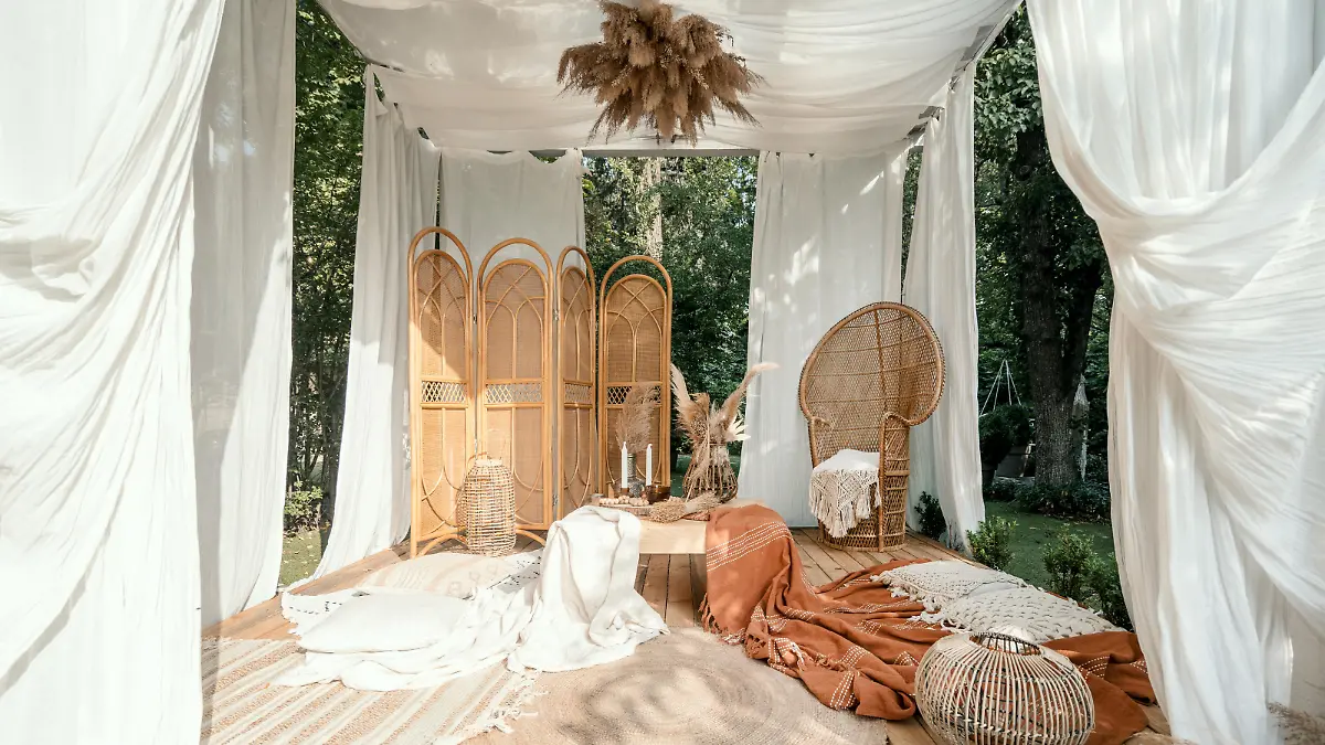 Garden arbour with rustic beige decoration, outdoor design. Wicker furniture outside in boho pergola, modern home backyard. Summer arbor with nature plant, wooden decor and blankets.