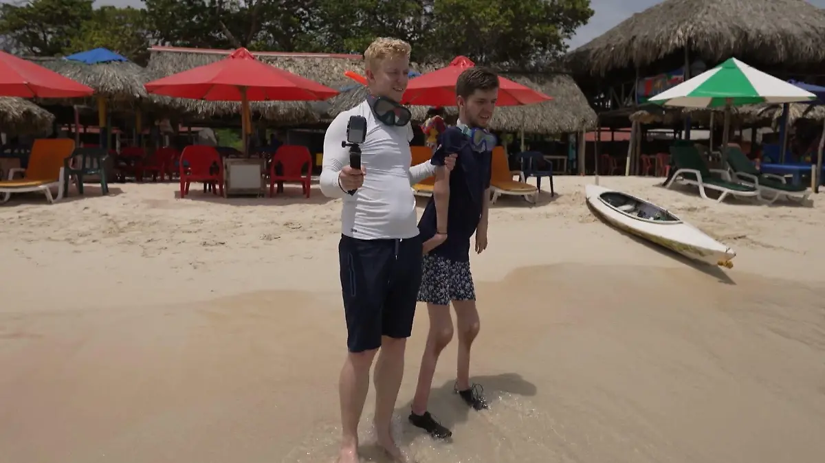 Ein junge greift dem anderen Jungen unter die Arme und hilft im am Strand ins Wasser zu gehen