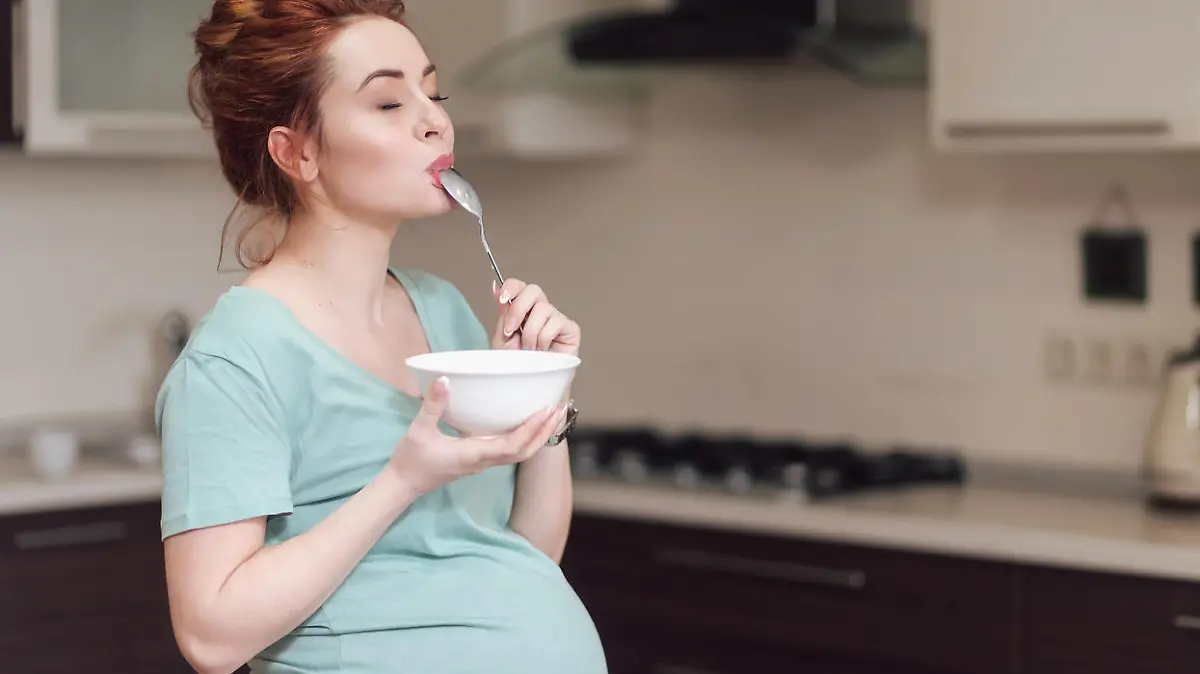Beautiful pregnant woman eating with lust cereals on breakfast, enjoying meal. Yummy food for pregnant ladies