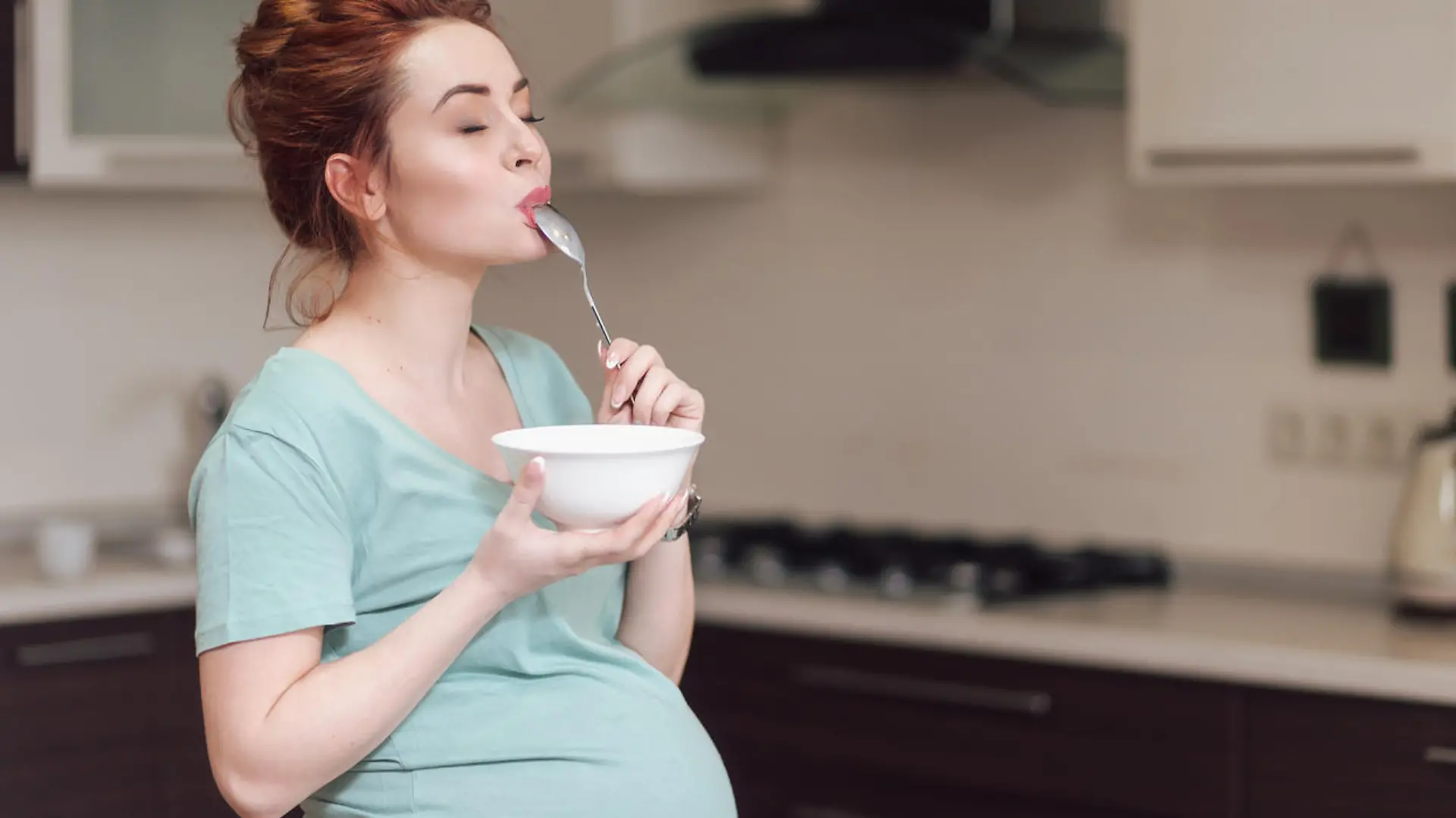 Beautiful pregnant woman eating with lust cereals on breakfast, enjoying meal. Yummy food for pregnant ladies