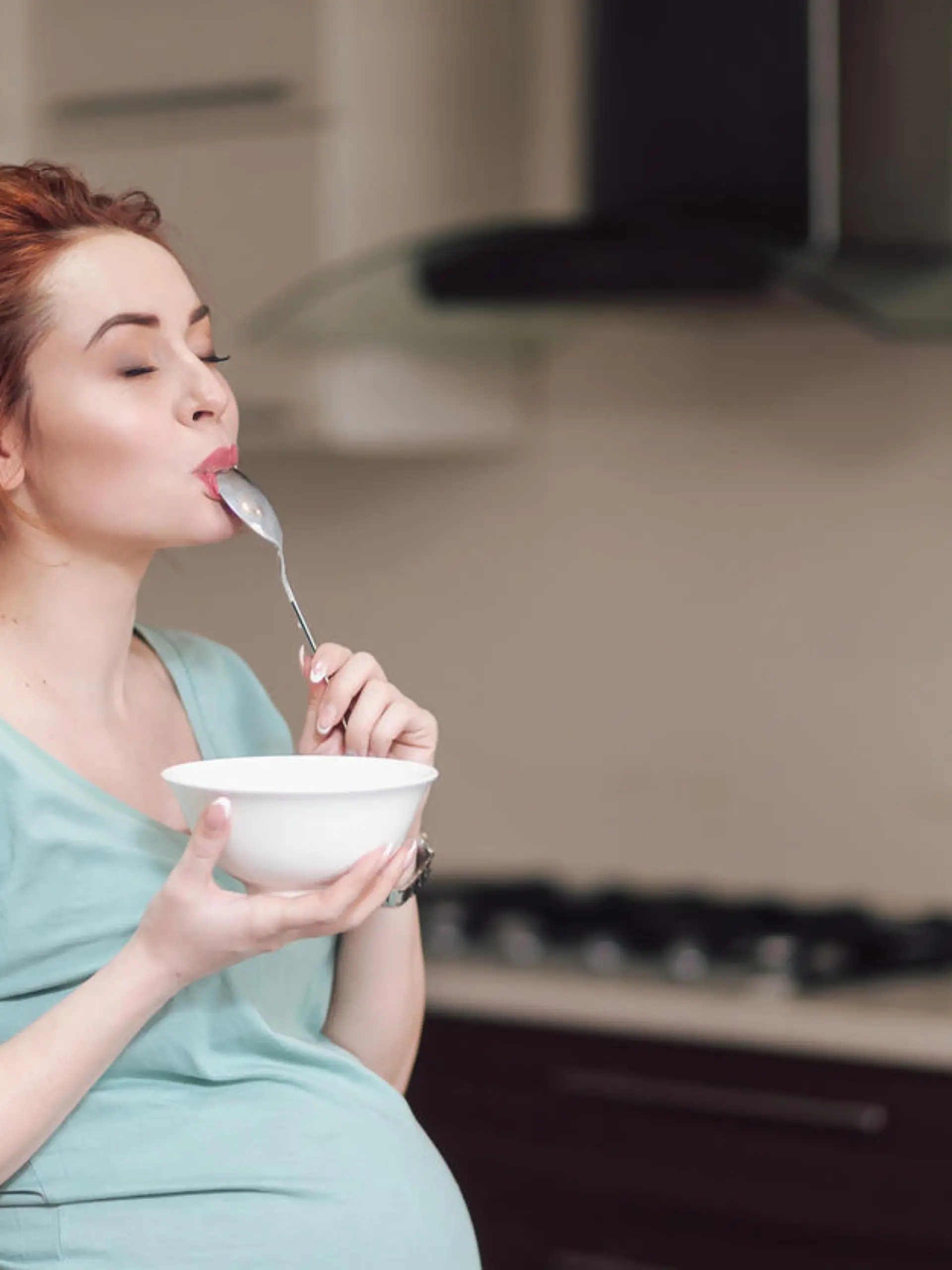 Beautiful pregnant woman eating with lust cereals on breakfast, enjoying meal. Yummy food for pregnant ladies