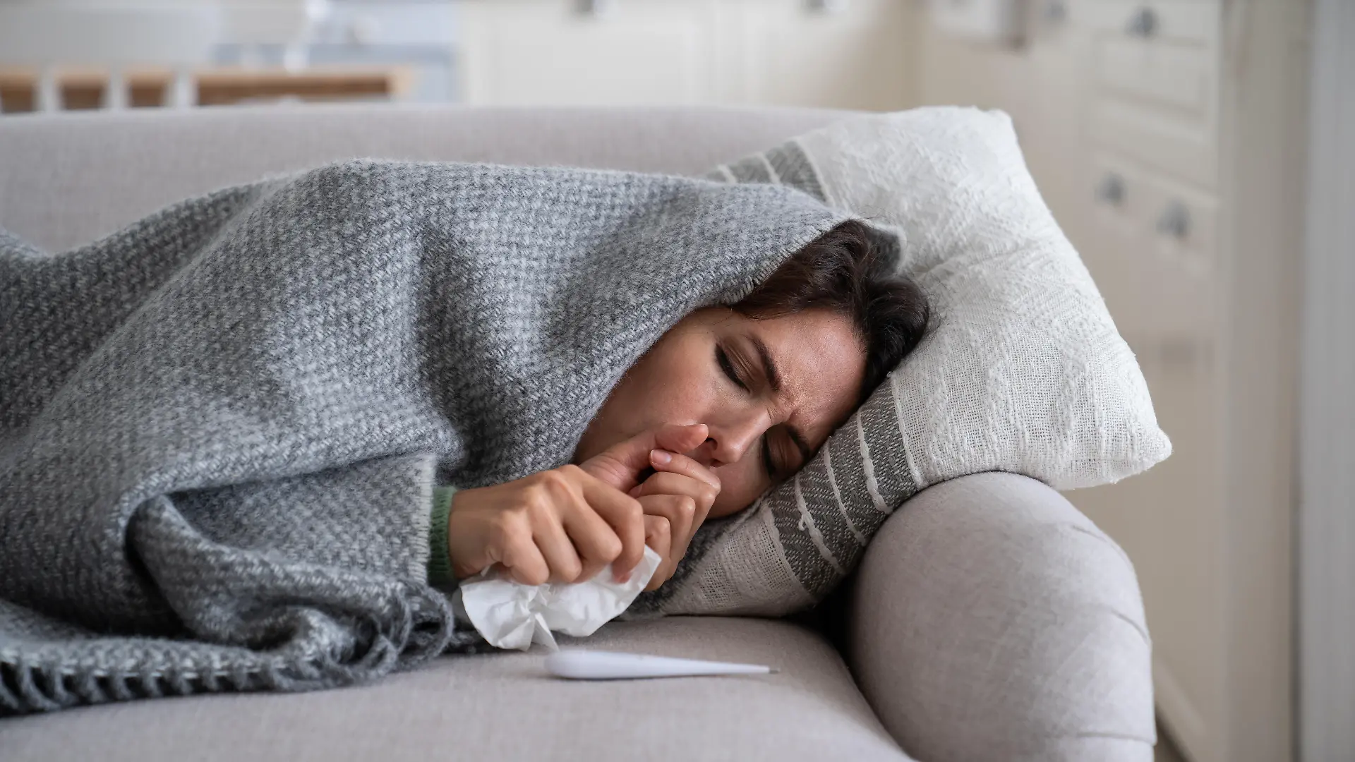 Frau liegt mit Schnupfen auf der Couch.