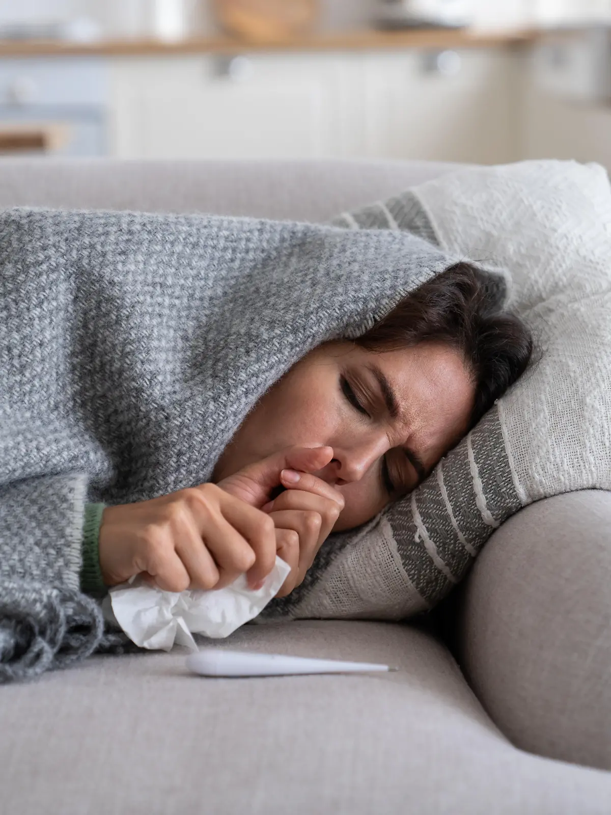 Frau liegt mit Schnupfen auf der Couch. 