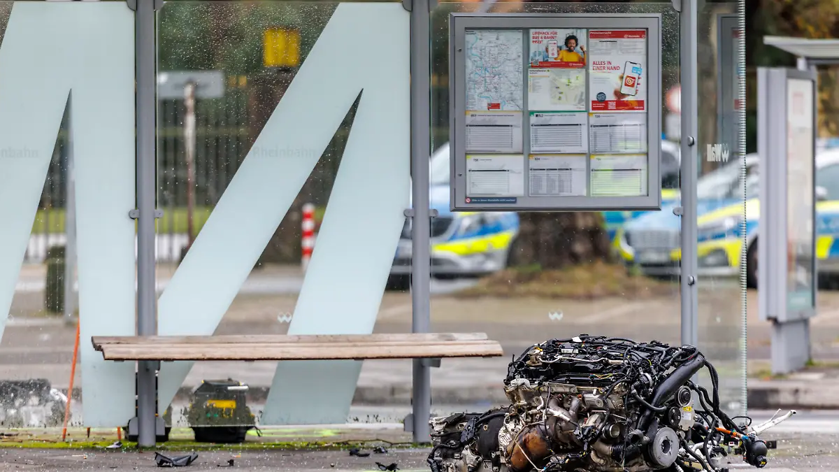 Der herausgerissene Motorblock des BMW liegt auf dem Gehweg vor einer Bushaltestelle in Düsseldorf-Golzheim