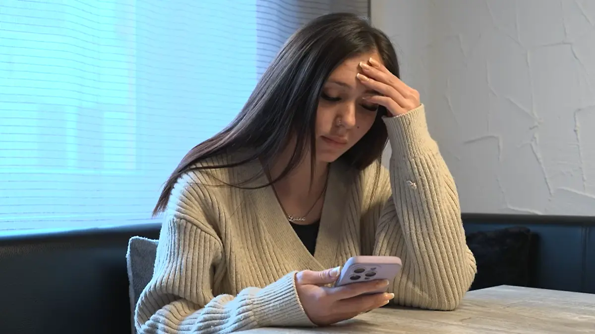 Giulia sitzt am Tisch mit ihrem Handy in der Hand.