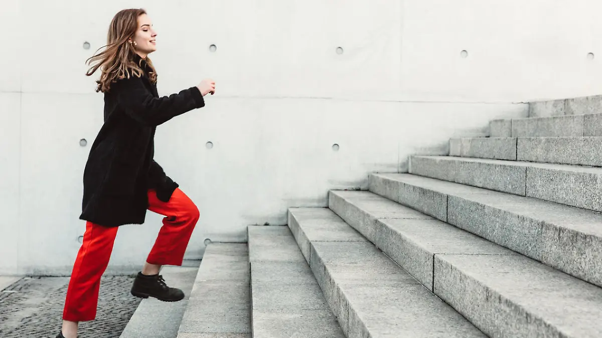 Young woman running up the steps outdoors. Woman in warm clothes climbing up the stairs.